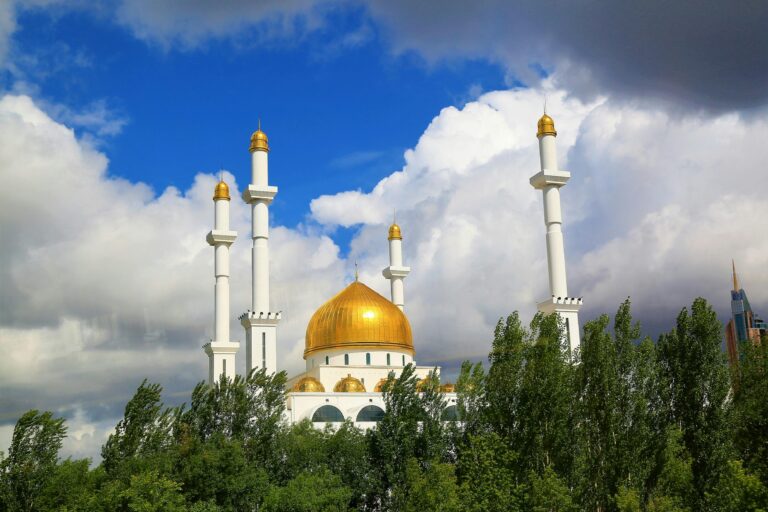 A stunning view of a grand mosque with a golden dome in Astana, Kazakhstan, under a vibrant blue sky.