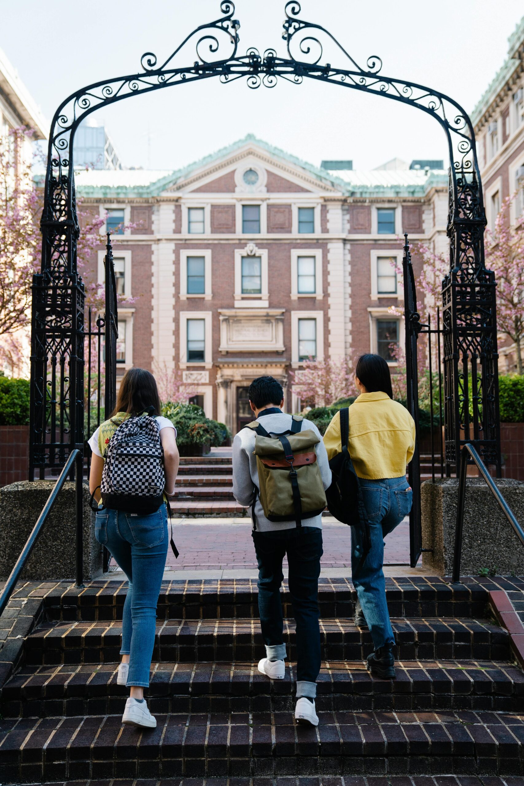 A group of students with backpacks walks towards a university building through an arch.